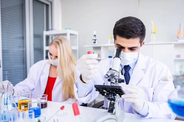 Científico masculino trabajando mirando al microscopio con la prueba de muestra tu — Foto de Stock