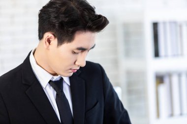 Neşeli, olgun, Asyalı genç bir iş adamının yanına git. Siyah ceketli ve beyaz gömlekli bir iş elbisesi giy. Ofis odasının arka planındaki pencereye bak..