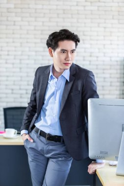 Portre başarılı, neşeli, yakışıklı Asyalı genç bir iş adamı ve bilgisayar ofis arka planında..