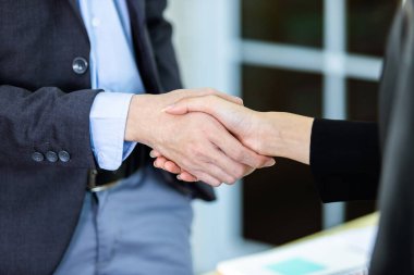 İş kadını ve işadamı, sözleşme imzalandıktan sonra ofis arka planında el sıkışırken, iş dünyası güven verici ve başarılı bir konsept olduğunu ifade etti.