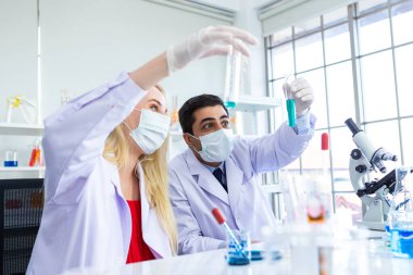 İki bilimadamı test tüpünü incelemek için kimya laboratuvarında çalışan bir bilim adamı ya da genç kadın ve erkek araştırmacı laboratuvar analizinde araştırma yapıyor.