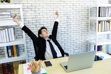 Dizüstü bilgisayardaki Asyalı genç iş adamının, bilgisayardaki akıllı telefonun ve defterdeki kalemin mutluluğu ofis odasının arka planında..