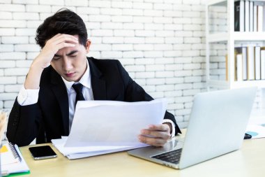 Stresli iş adamı dizüstü bilgisayarla çalışıyor ve ofis odasındaki kayıplardan sonra baş ağrısı çekiyor..