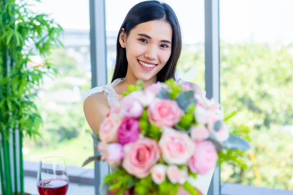 バレンタインデーのコンセプト 笑顔の幸せアジアの若い女性がテーブルフードショーに座ってレストランの背景にバラの花束を持っている — ストック写真