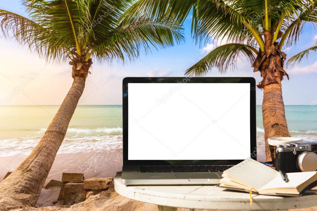 Mockup of laptop computer with empty screen with camera,notebook,coffee cup on table at landscape early sunrise over blue the sea background,working on the beach,Freelance work and holiday traveler.
