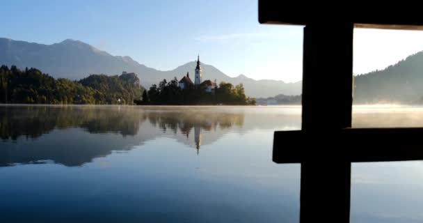 Bled νησί με προσκύνημα εκκλησία της Κοίμησης της Θεοτόκου και Bled κάστρο στη λίμνη Bled στο σαφές πρωί του φθινοπώρου με ελαφριά ομίχλη — Αρχείο Βίντεο