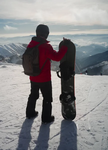 Snowboarder debout sur un rocher au bord d'une falaise et regardant vers le bas . — Photo