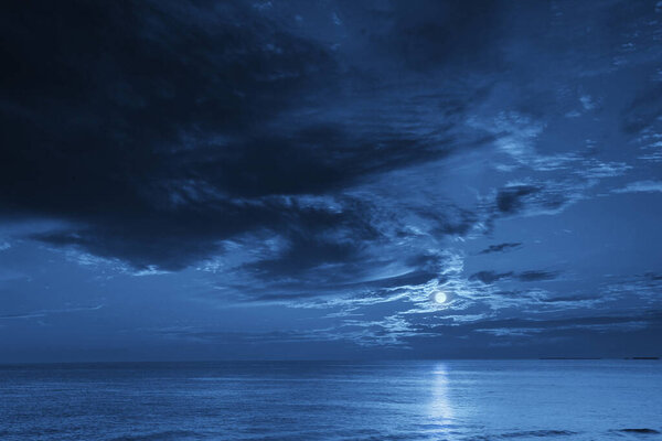 This photo illustration of a deep blue moonlit ocean at night with calm waves would make a great travel background for any coastal region or vacation, emphasizing the beauty of the night time ocean or sea.