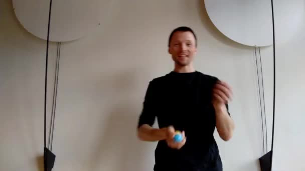 Homme talentueux jonglant avec des boules de couleur avant mur blanc . — Video