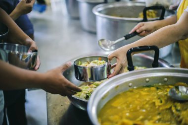 Gönüllülerden bedava hayır yemeği alabilmek için bir konteynırı tutan ihtiyaç sahiplerinin elleri: gıda yardımı kavramı.