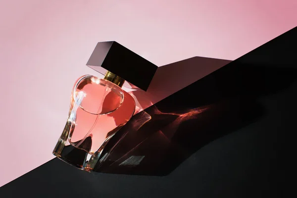 Бутылка духов на розовом и черном фоне — стоковое фото