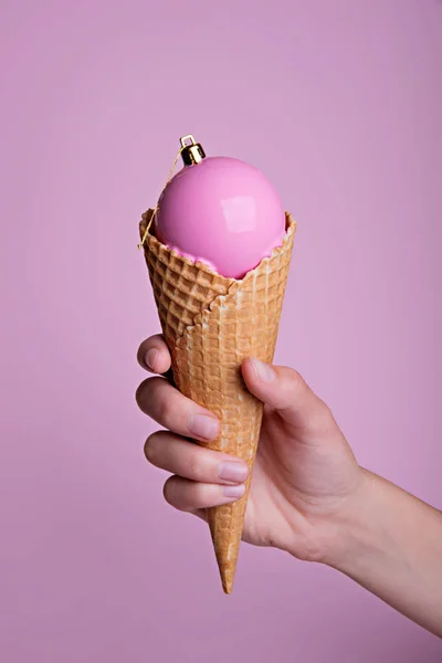 Female hand holding ice cream waffle cone with christmas ball in it. — Stock Photo, Image