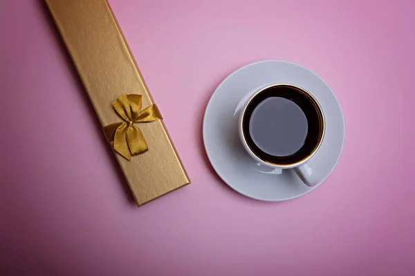 Cup of coffee and gift box on a pale pink background.