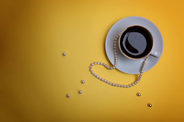 Sarı arka planda bir fincan espresso ve inci boncuklar..