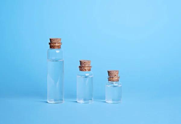 Botellas pequeñas con líquido o aceite sobre fondo azul . — Foto de Stock