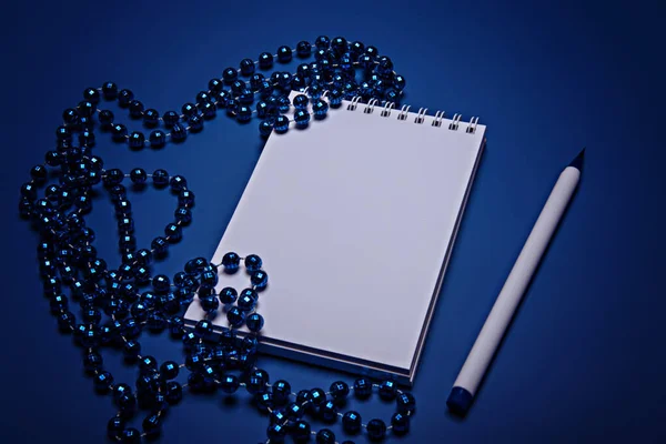 Mavi Noel boncukları, mavi bir arka planda defter ve kalem..