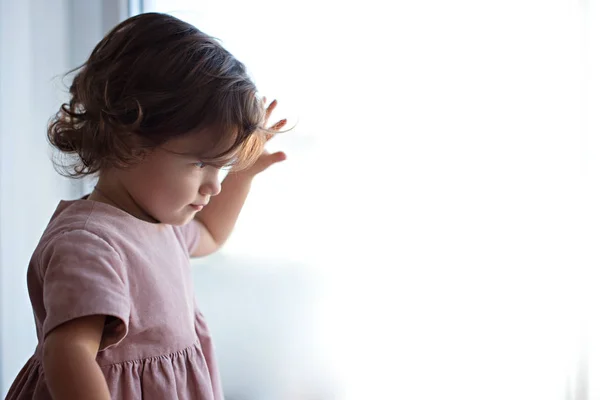 Little girl looks out the window and touches the glass with her fingers.