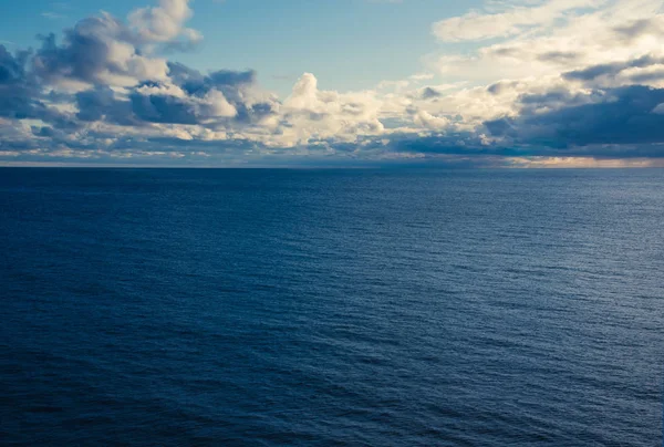 Γαλάζια επιφάνεια του ωκεανού και πυκνό πυκνό πυκνό λευκό και γκρι σύννεφα σε ένα γαλάζιο ουρανό. — Φωτογραφία Αρχείου