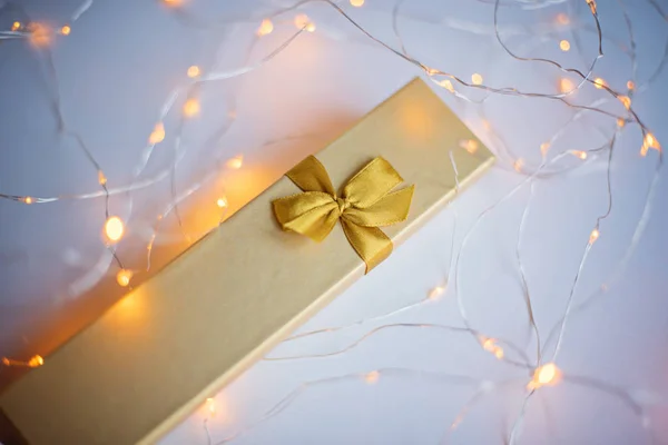 Caixa de presente dourada em uma grinalda luminosa . — Fotografia de Stock