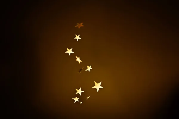 Gold stars are falling on a dark brown background.