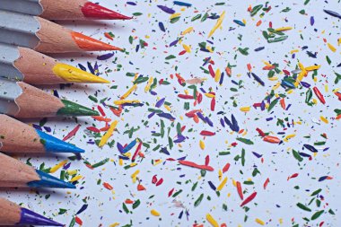 Beyaz kağıt üzerinde kalemler ve çok renkli talaşlar..