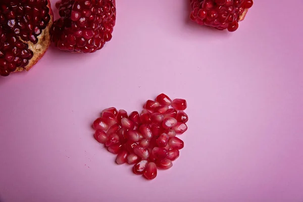 Семена граната на розовом фоне. Форма сердца . — стоковое фото
