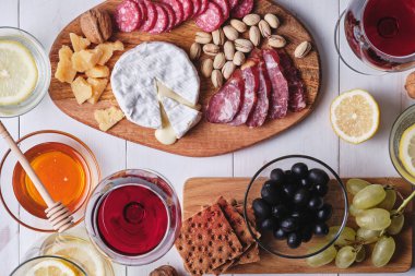 Romantik bir akşam yemeği için lezzetli ürünler. Peynir ve sosis lezzetleri, fındık, meyve, zeytin, ekmek, üzüm, şarap ve bal eski beyaz ahşap bir masada. Üst görünüm.