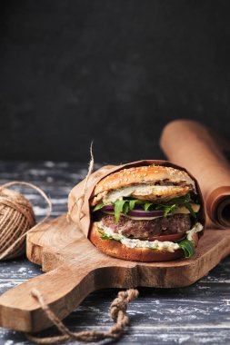 close up of mouth-watering burger with grilled beef patty and fresh vegetables. Tasty american cheeseburger on wooden board. 