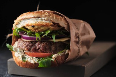 close up of mouth-watering burger with grilled beef patty and fresh vegetables. Tasty american cheeseburger on wooden board. 