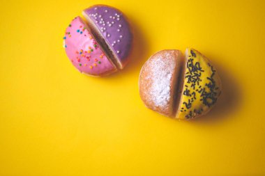 Dilimlenmiş, doldurulmuş donutların yakın plan çekimleri. Sarı kağıdın arka planında renkli jölelerle süslenmiş. Üst görünüm.