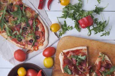 İki ev yapımı İtalyan pizzası: acılı baharatlı ve füme sosisli; zeytinli baharatlı ve iki çeşit sosisli. Servis yapmadan önce panoda İtalyan yemeği var..