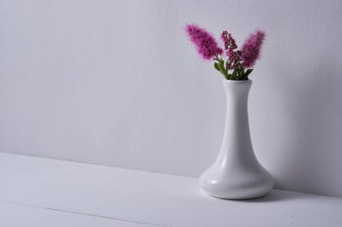 Beyaz ahşap bir masada, beyaz bir vazoda çiçekler.