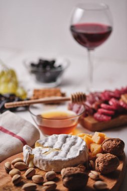Romantik bir akşam yemeği için lezzetli ürünler. Camembert ve Parmesan peyniri, sosis, fındık, meyve, zeytin, ekmek, üzüm, şarap ve bal eski beyaz ahşap bir masada. Üst görünüm.