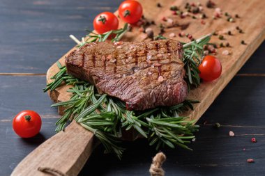 Biberiye dallarında taze pişmiş biftek. Büyük ahşap bir tahtada servis edilmiş, kiraz domatesli..