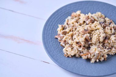 Gri tabakta yakın plan mantarlı risotto. Beyaz ahşap bir masada İtalyan yemeği.