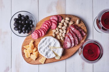 Peynir ve sosis lezzetleri, fındıklar, eski beyaz ahşap bir masada şarap bardakları. Romantik bir akşam yemeği ve şarap. Üst görünüm.