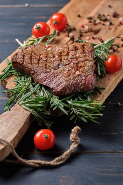 Biberiye dallarında taze pişmiş biftek. Tabak kiraz domatesli büyük ahşap bir tahtanın üzerinde servis edildi. Yakın plan..