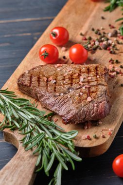 Biberiye ve kiraz domatesli ahşap bir tahtanın üzerinde taze pişmiş biftek. Yakın plan..