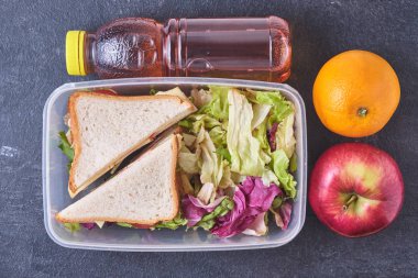 Okul kahvaltısı. Plastik bir kabın içinde iki sandviç ve bir salata, bir elma, bir portakal ve meyve suyu çocuğun okul yemeği için hazırlanır..