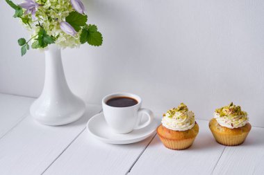 Kahvaltı için kahve ve meyveli kek. Sabah masasında tatlı, espresso ve beyaz ahşap bir masada vazoda çiçekler..