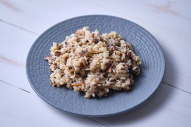 Gri tabakta yakın plan mantarlı risotto. Beyaz ahşap bir masada İtalyan yemeği.