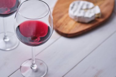 Beyaz ahşap bir masada bir bardak şarap ve peynirli peynir. Romantik bir akşam yemeği hazırlıyorum..