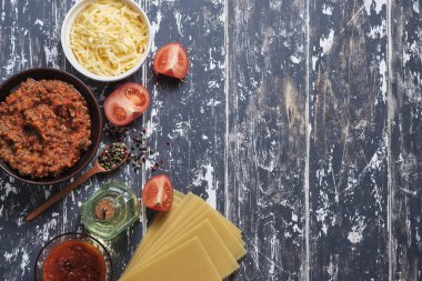 Eski ahşap mutfak masasında lazanya pişirmek için gerekli malzemeler: peynir, makarna, sos, domates, kıyma, tereyağı, biber.. 