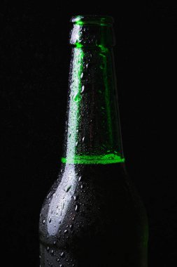 Soğuk bir bira şişesi ve siyah bir arka planda biraz su..