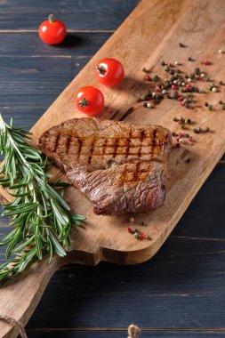 Biberiye ve kiraz domatesli ahşap bir tahtanın üzerinde taze pişmiş biftek. Yakın plan..