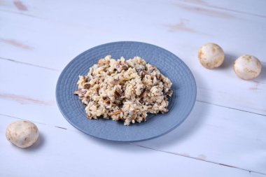 Gri tabakta yakın plan mantarlı risotto. Beyaz ahşap bir masada İtalyan yemeği.
