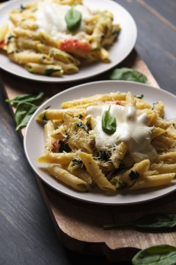 İki porsiyon domatesli makarna, ıspanak, parmesan ve bolonez sosu büyük bir mutfak tahtasında. Tabakta, ahşap bir masada..