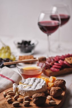 Romantik bir akşam yemeği için lezzetli ürünler. Camembert ve Parmesan peyniri, sosis, fındık, meyve, zeytin, ekmek, üzüm, şarap ve bal eski beyaz ahşap bir masada. Üst görünüm.