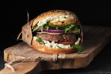 close up of mouth-watering burger with grilled beef patty and fresh vegetables. Tasty american cheeseburger on wooden board. 