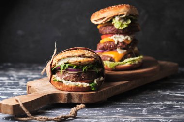 close up of mouth-watering burger with grilled beef patty and fresh vegetables. Tasty american cheeseburger on wooden board. 
